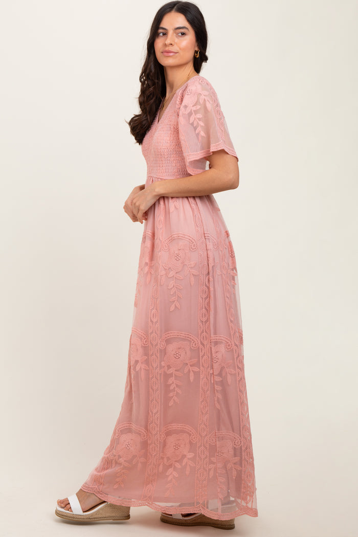woman wearing a dusty pink maxi dress with floral embroidery and short sleeves, posing sideways against a neutral background