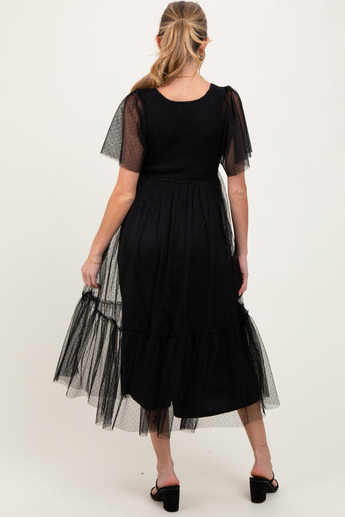 woman wearing a black maternity dress with short sheer puff sleeves and a tiered tulle hem, showing her baby bump