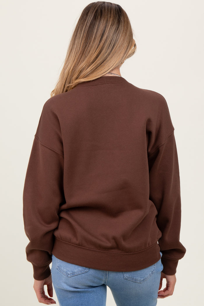 woman wearing a brown oversized maternity sweatshirt, view from the back, styled with light blue jeans