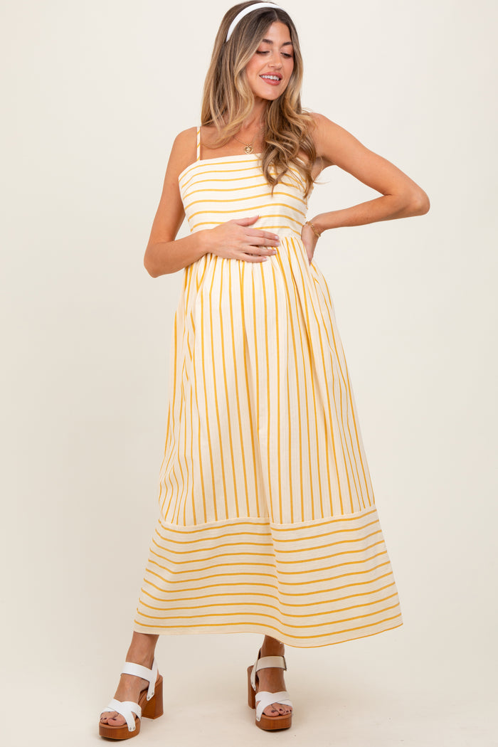 woman wearing a yellow and white striped maternity maxi dress and holding her baby bump
