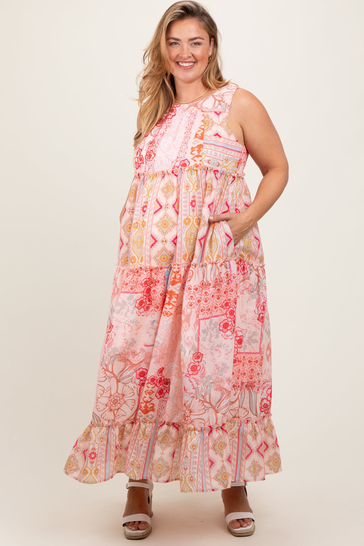 woman wearing a pink patterned maternity plus maxi dress with pockets and ruffled hem, showing her baby bump