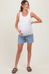 woman wearing a white ribbed maternity tank top and denim maternity shorts, showcasing her baby bump