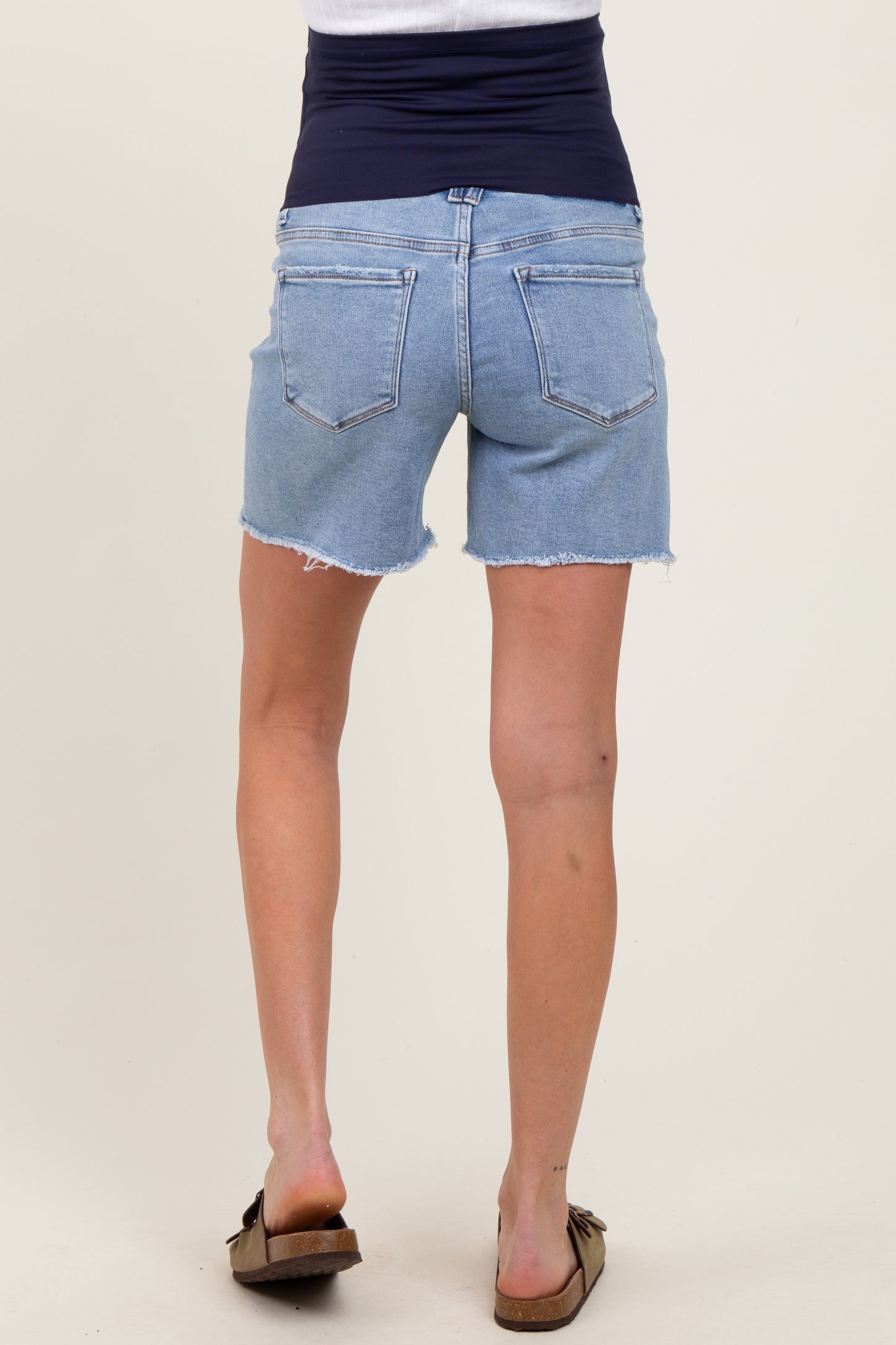 woman wearing a pair of light blue maternity denim shorts with a frayed hem and a stretchy navy waistband