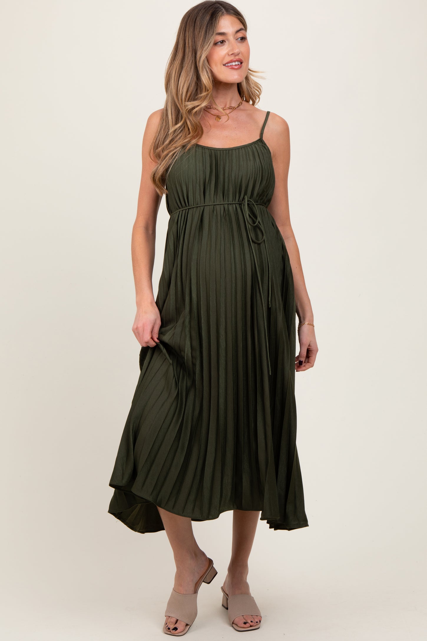 woman wearing an olive green pleated maternity dress with a tie waist and adjustable spaghetti straps