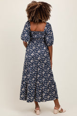 woman wearing a navy blue floral maternity dress with puff sleeves and a tiered skirt