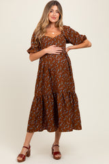 woman wearing a brown floral maternity dress with puff sleeves and tiered skirt, gently holding her baby bump