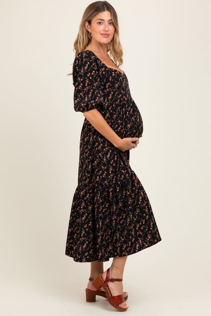 woman wearing a black floral maternity dress with a ruffled hem and holding her baby bump
