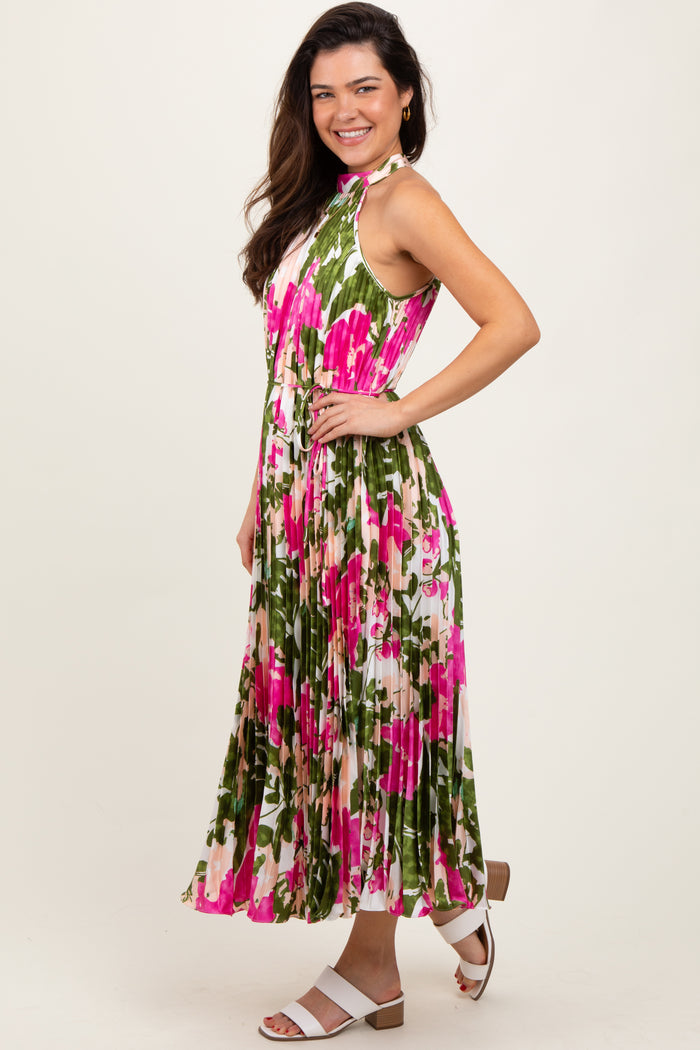 woman wearing a floral pleated maxi dress with pink and green hues, posing with one hand on her hip