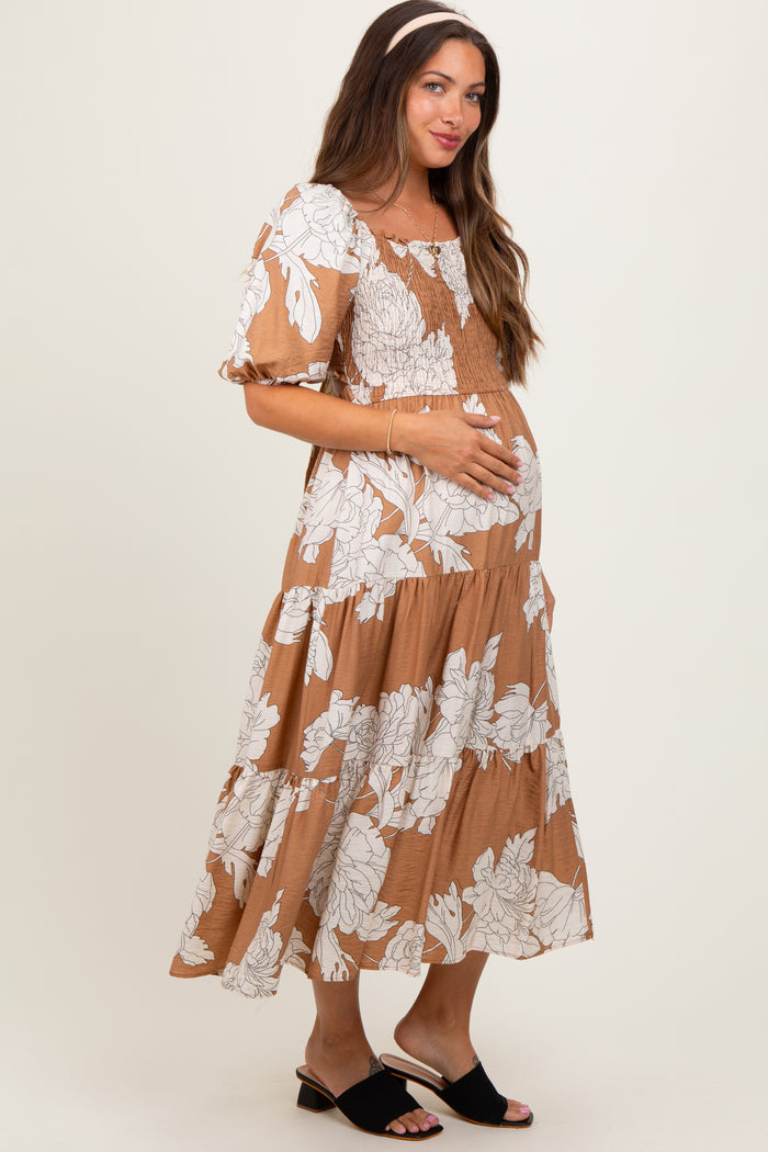woman wearing a brown floral maternity dress with puff sleeves and holding her baby bump