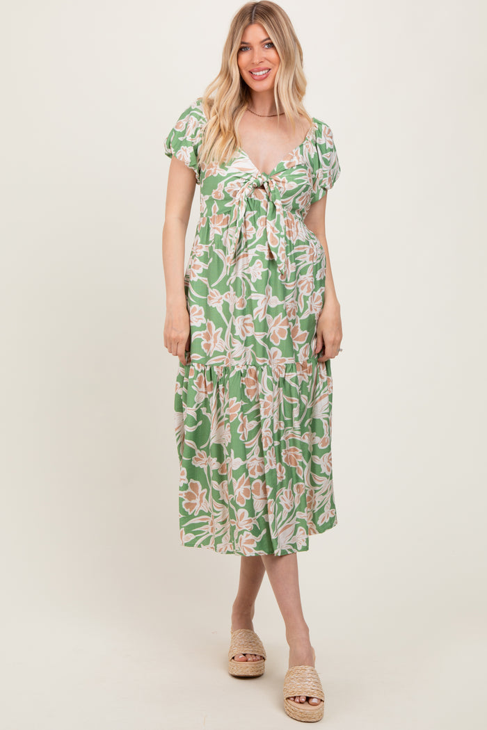 woman wearing a green floral midi dress with a tie front and puff sleeves, standing and smiling
