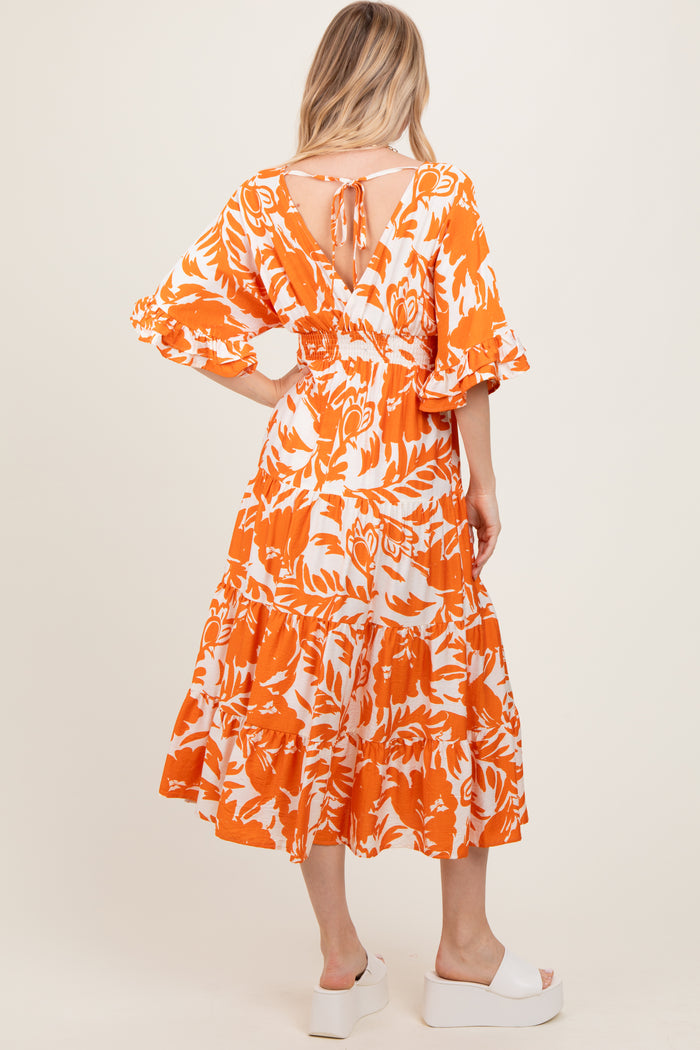 woman wearing an orange floral print maxi dress with puff sleeves and a tie-back detail