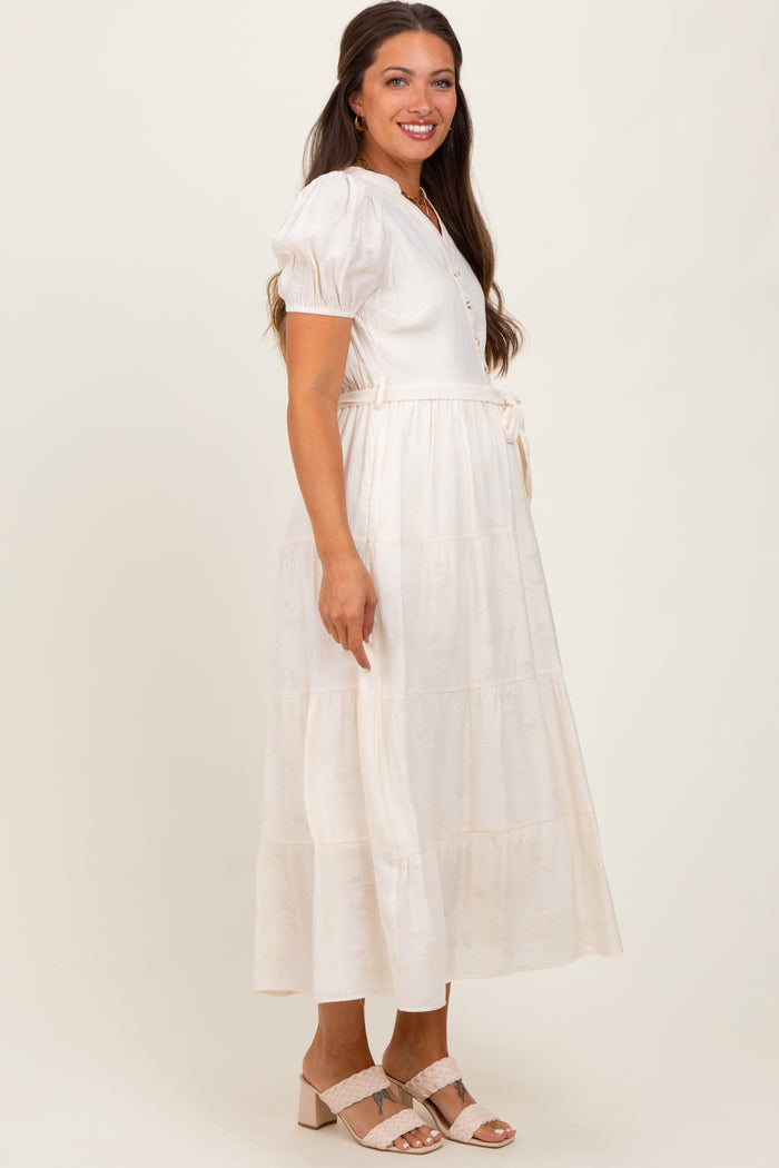 woman wearing a cream maternity midi dress with puff sleeves and a tie waist, featuring a tiered skirt and button details
