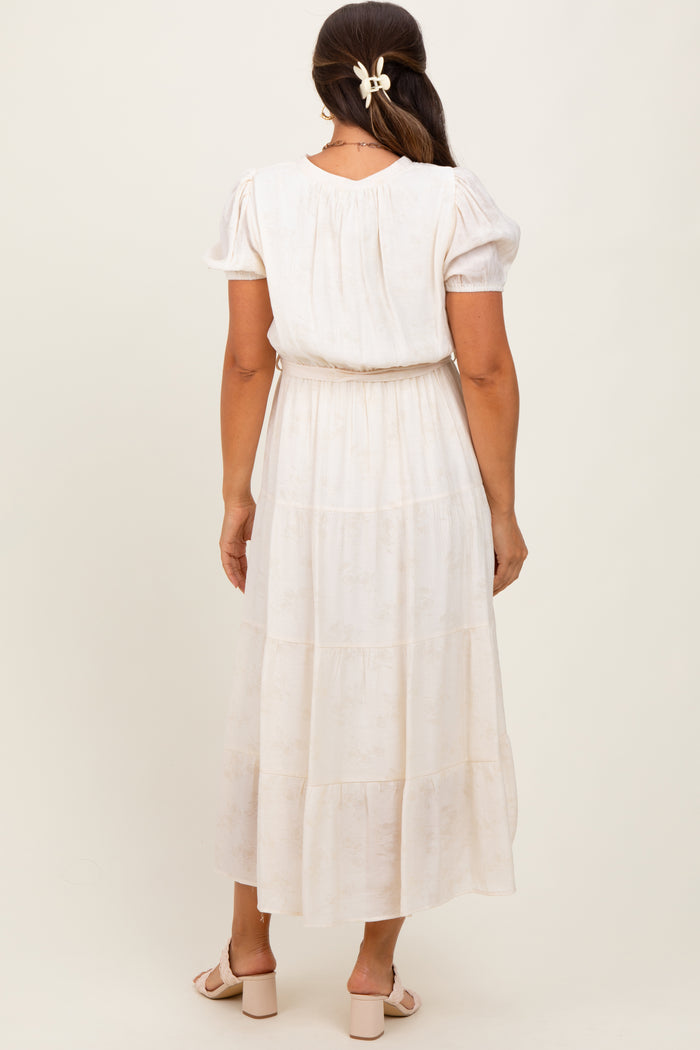 woman wearing a light cream maternity dress with puff sleeves and a tiered skirt, showing her baby bump from the back