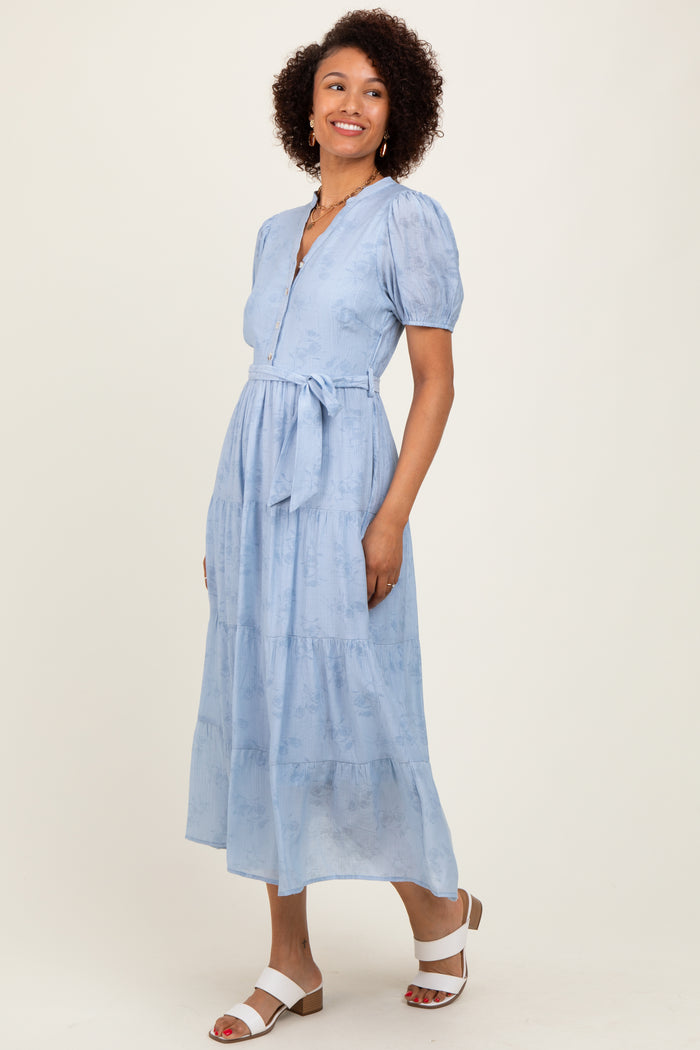 woman wearing a light blue puff sleeve maxi dress with a belt and button details, standing and smiling