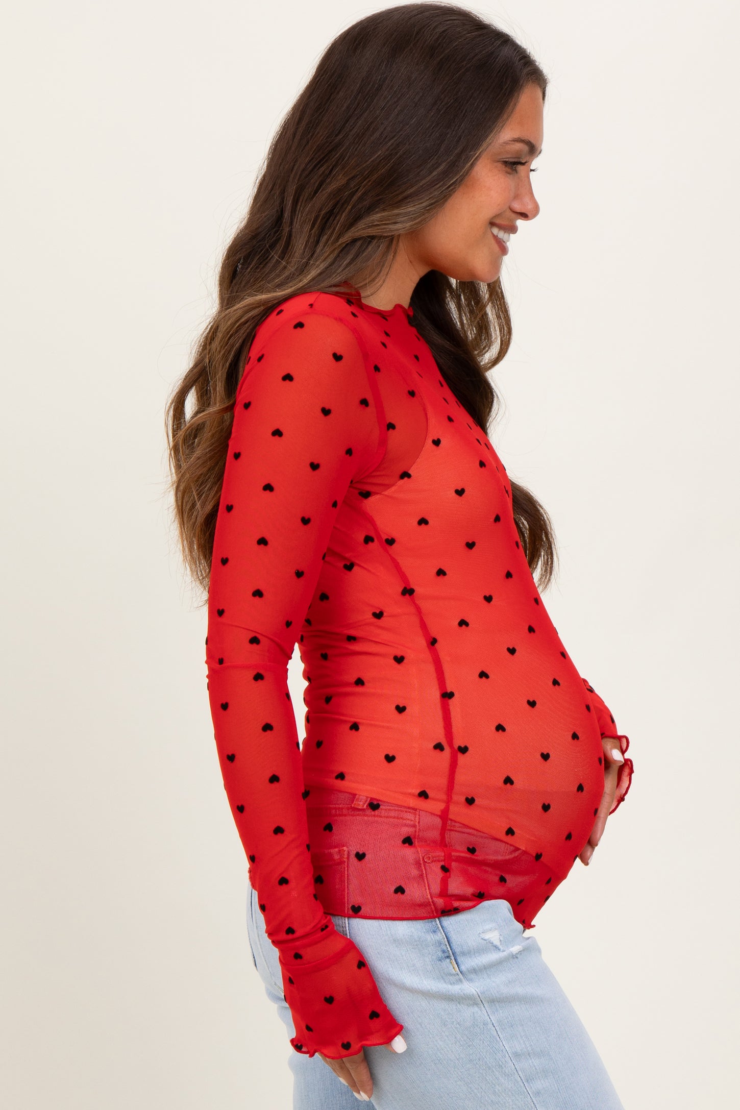 woman wearing a red sheer long sleeve maternity top with black heart patterns and showing her baby bump