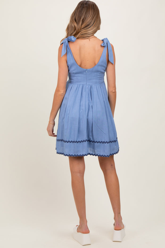 woman wearing a blue maternity dress with tie straps and scalloped hem, shown from the back