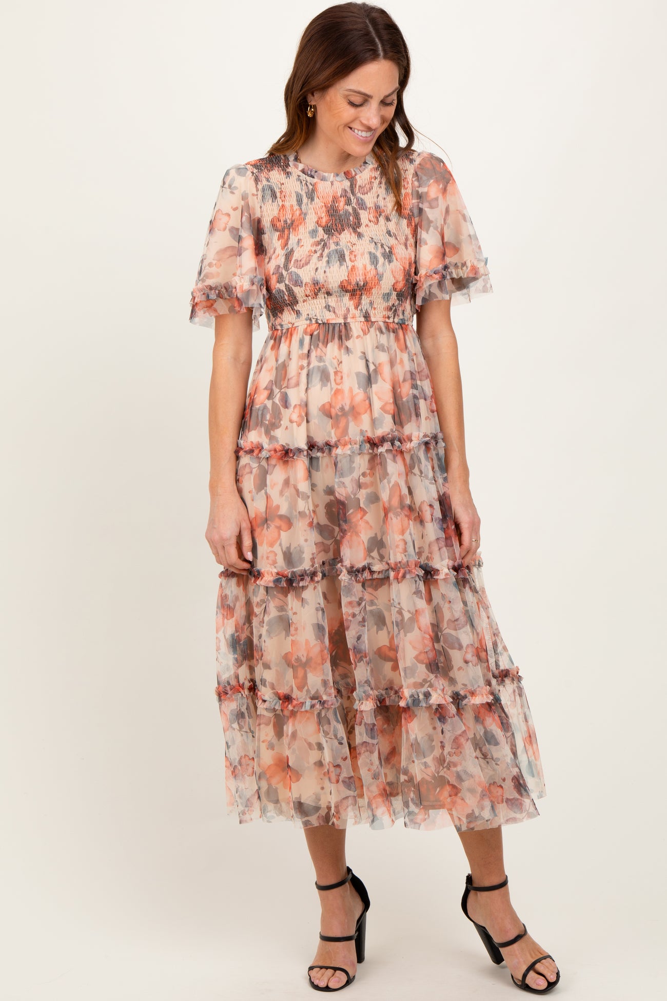 woman wearing a floral tiered maxi dress with ruffled sleeves and a smocked bodice, standing and smiling