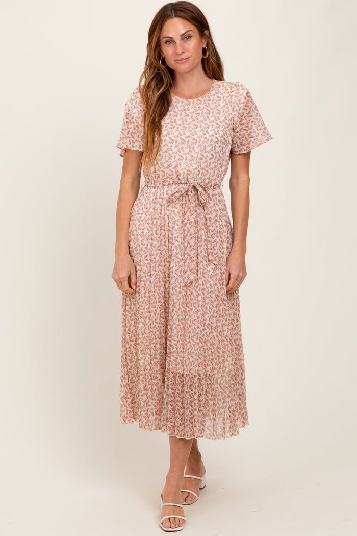 woman wearing a light pink floral midi dress with short sleeves and a tie belt at the waist