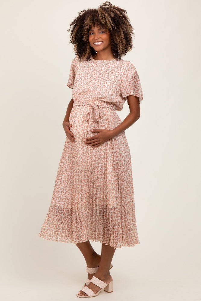 woman wearing a pink floral maternity dress with a tie waist, holding her baby bump and smiling