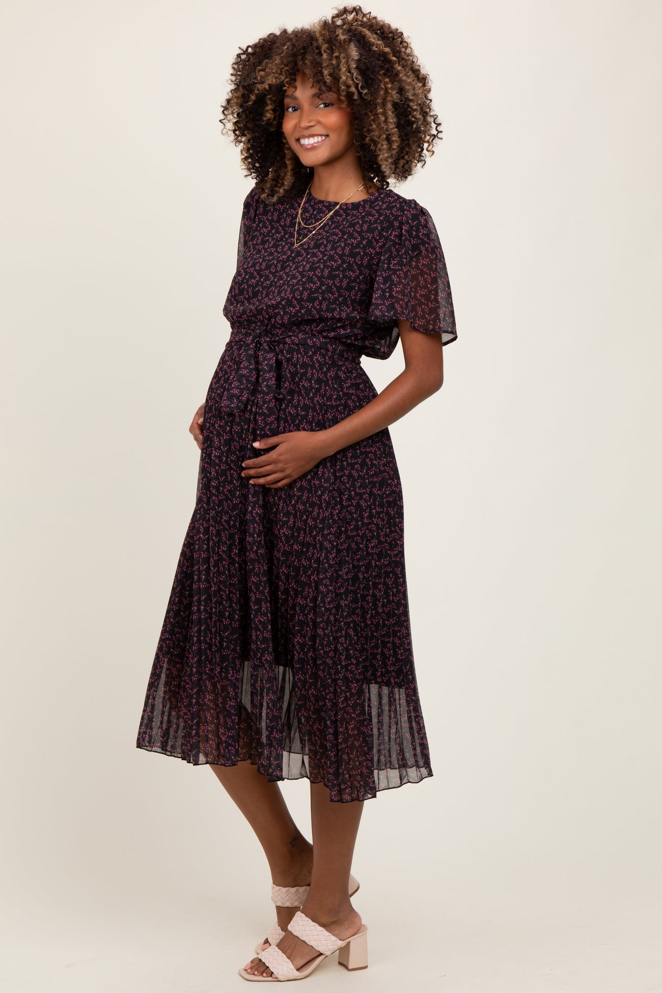 woman wearing a black floral print maternity dress with short sleeves and a tie waist, showing her baby bump
