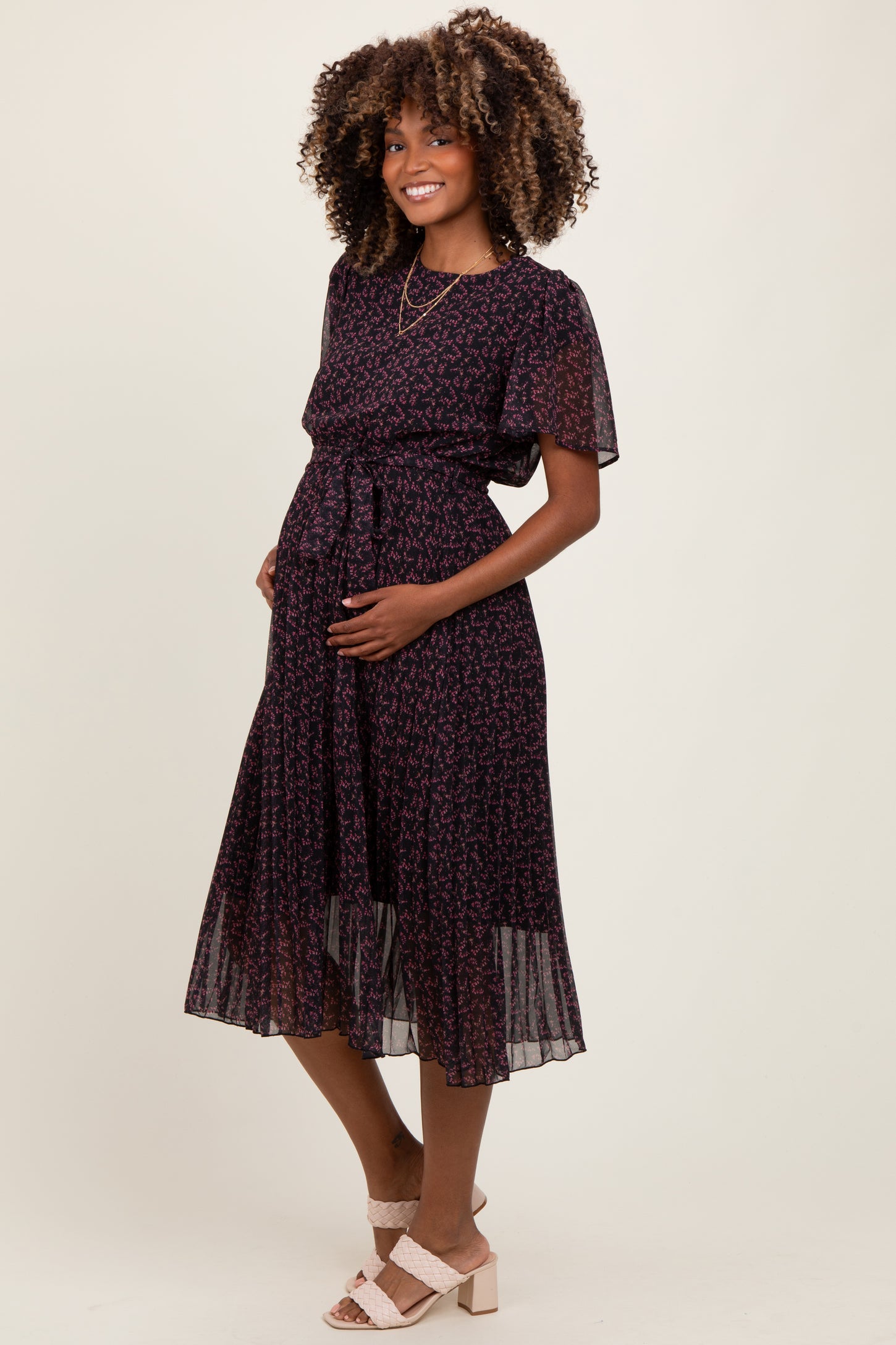 woman wearing a black floral print maternity dress with short sleeves and a tie waist, showing her baby bump