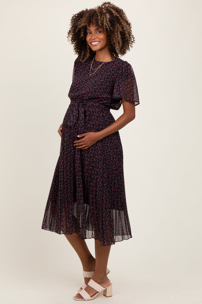 woman wearing a black floral print maternity dress with short sleeves and a tie waist, showing her baby bump