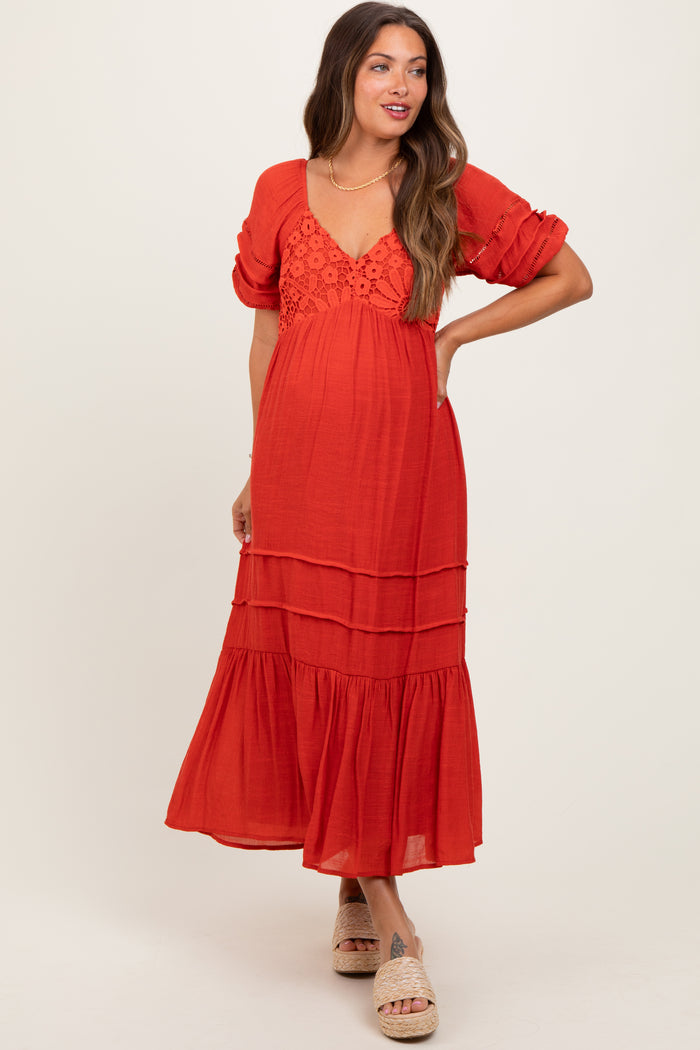 woman wearing a red maternity dress with a tiered design and lace detail, posing with one hand on her hip