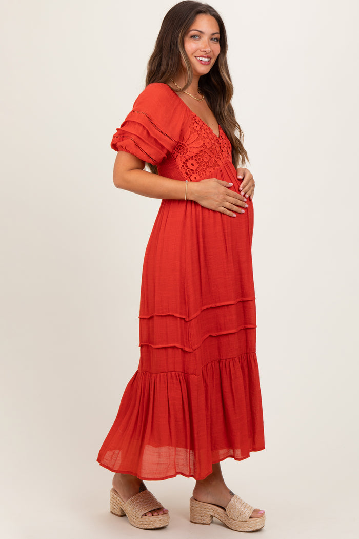 woman wearing a red tiered maternity dress with short ruffled sleeves and a crochet detail, cradling her baby bump