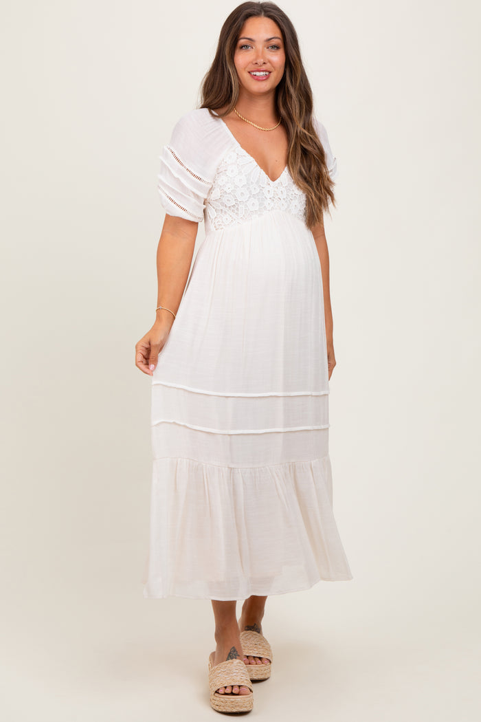 woman wearing a white maternity maxi dress with puff sleeves and lace details, showcasing her baby bump
