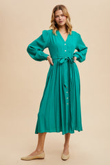 woman wearing a teal long sleeve button-up dress with a cinched waist and flowing skirt