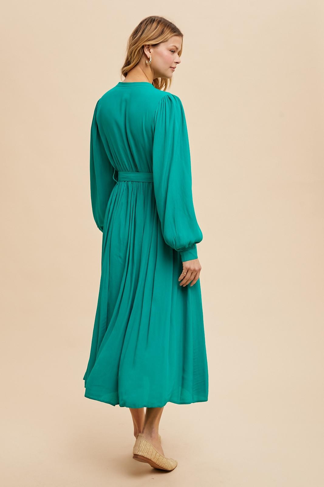 woman wearing a teal long sleeve maxi dress with a cinched waist and flowing skirt, viewed from the back