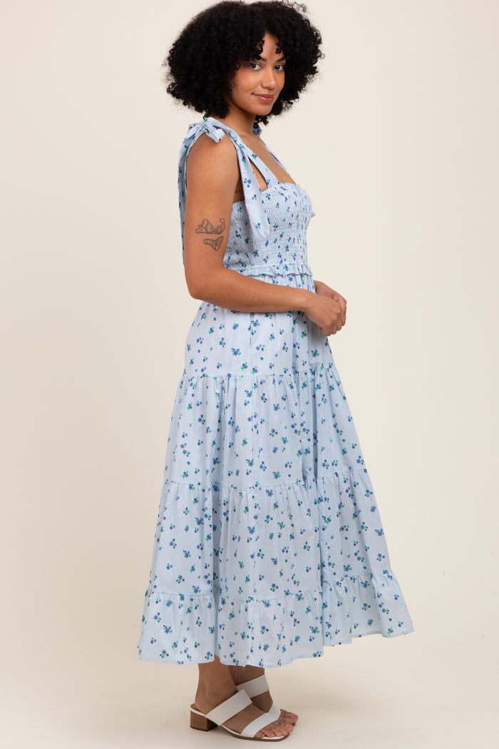 woman wearing a light blue floral midi dress with adjustable tie straps and a tiered skirt