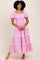 woman wearing a pink striped maxi dress with puff sleeves and ruffled tiers, standing against a neutral background