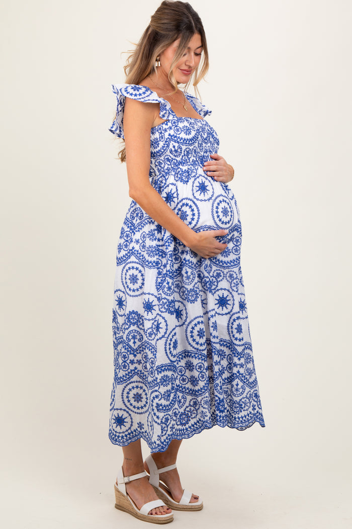 woman wearing a blue and white patterned maternity dress, holding her baby bump, with ruffled straps and a flowy hem