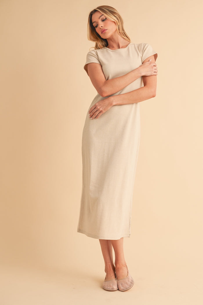 woman wearing a beige short sleeve maxi dress with a slightly fitted silhouette and side slits