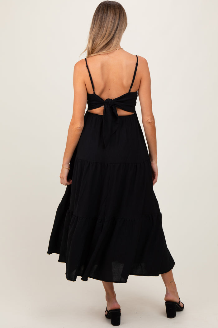 woman wearing a black maternity maxi dress with a tie-back detail and tiered skirt, showing a baby bump