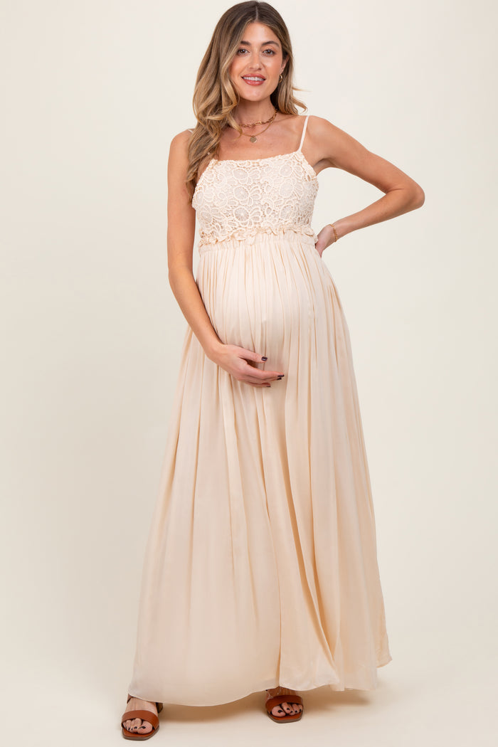 woman wearing a light beige maternity maxi dress with a lace bodice and holding her baby bump