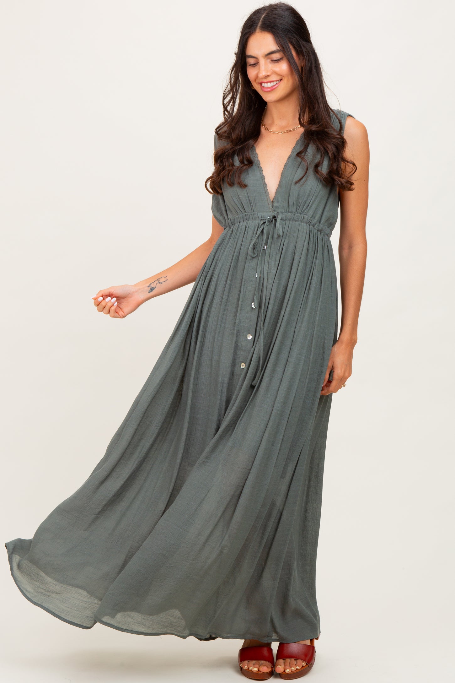 woman wearing a flowy olive green maxi dress with a deep v-neck and button details, standing gracefully