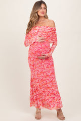 woman wearing a pink floral off-the-shoulder maternity dress and cradling her baby bump
