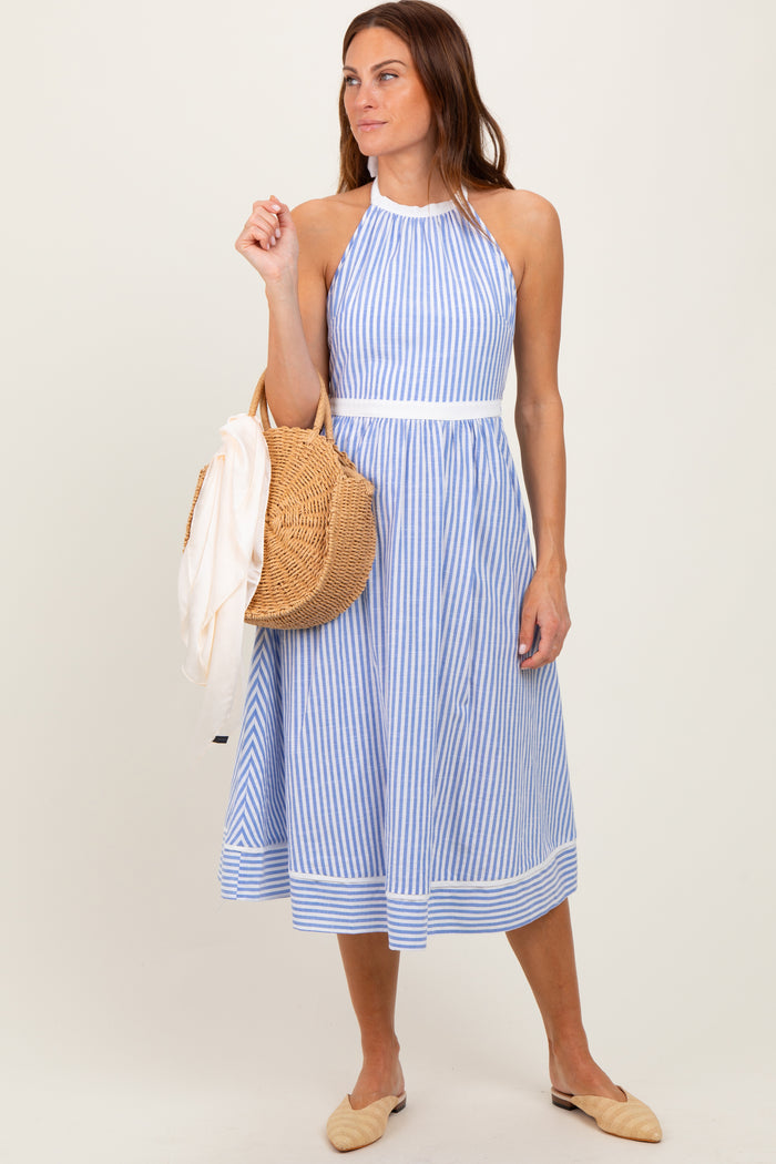 woman wearing a blue and white striped halter neck sundress and holding a straw bag