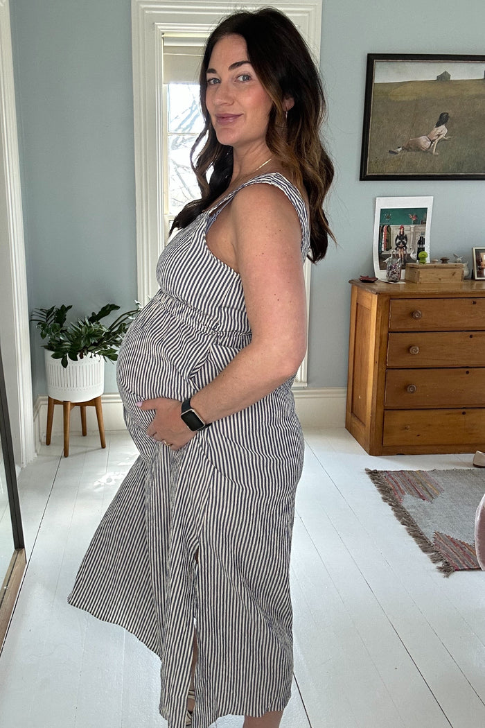 woman wearing a striped maternity dress, holding her baby bump in a cozy home setting