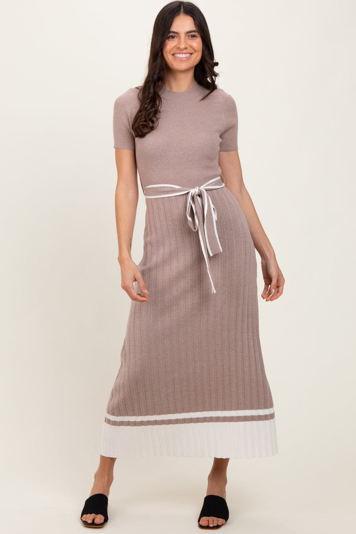 woman wearing a beige ribbed maxi dress with a tie belt and contrasting white hem detail, standing in a relaxed pose