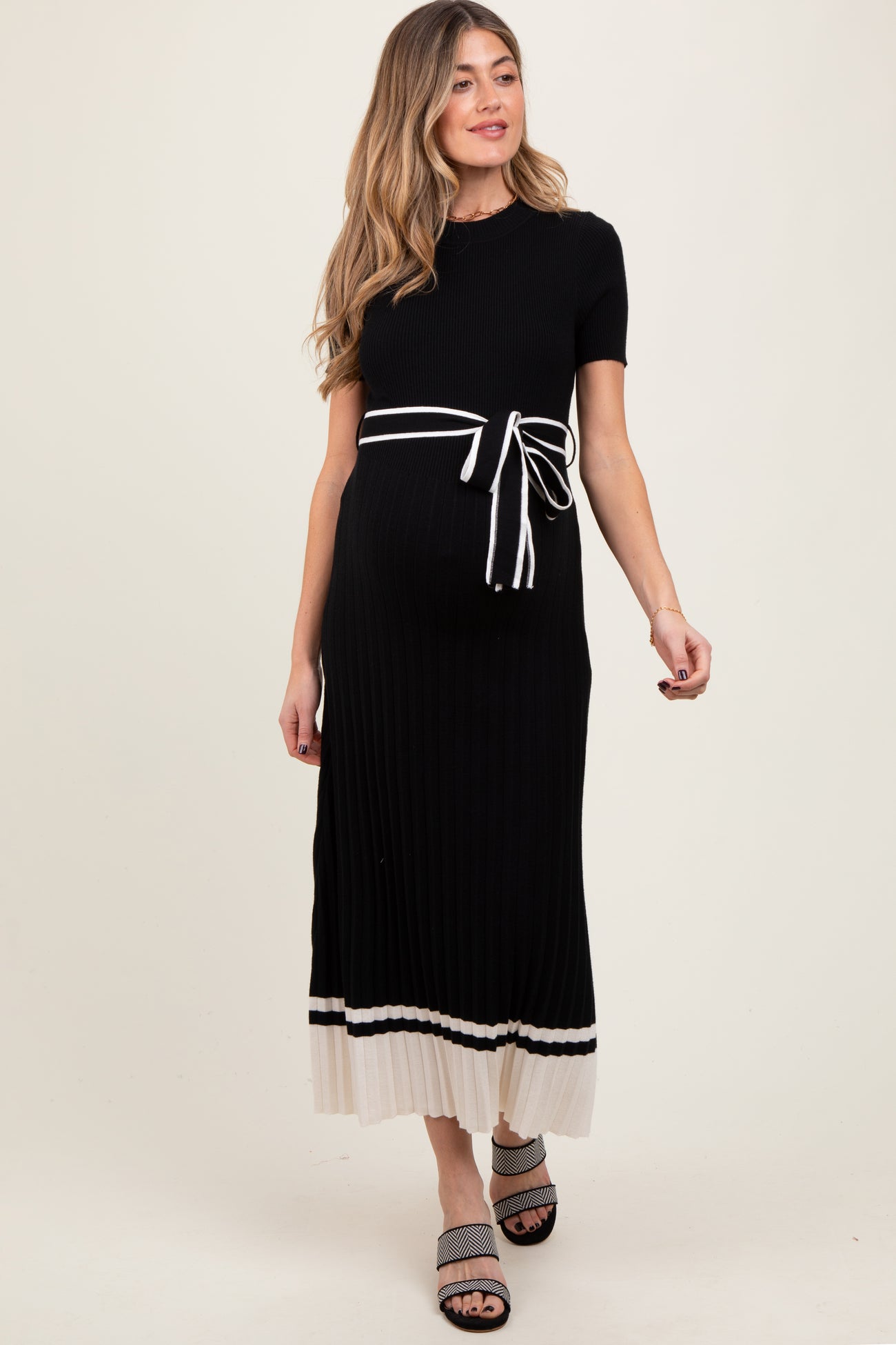 woman wearing a black ribbed maternity dress with a tied waist and cream striped hem, showcasing her baby bump