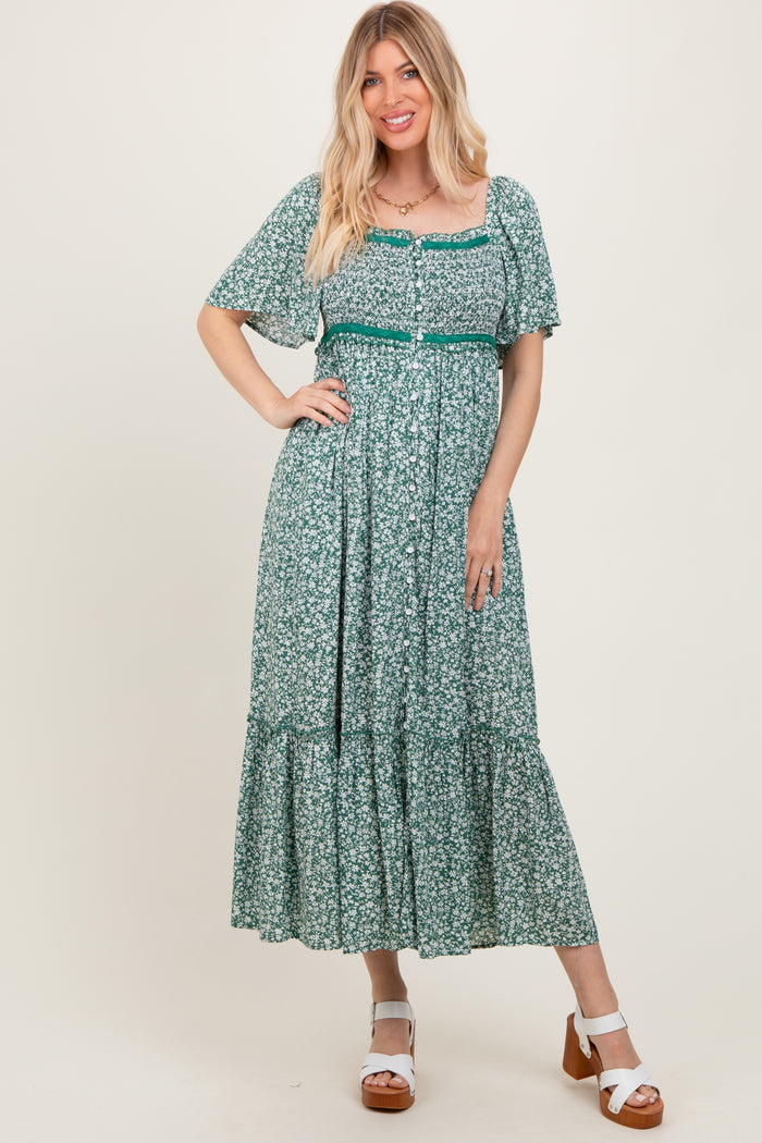 woman wearing a green floral maxi dress with short sleeves and a tiered skirt, standing on a neutral background