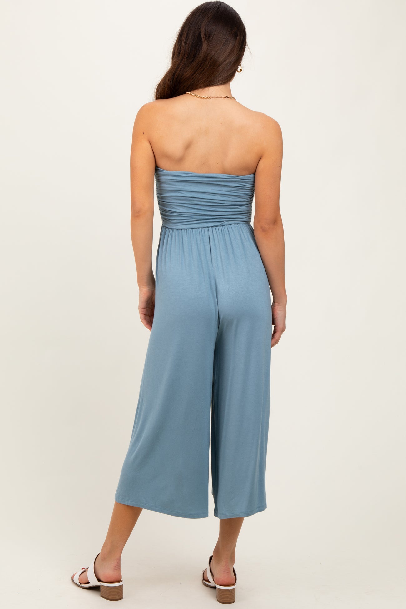 woman wearing a back view of a light blue strapless jumpsuit with a fitted bodice and wide-leg pants