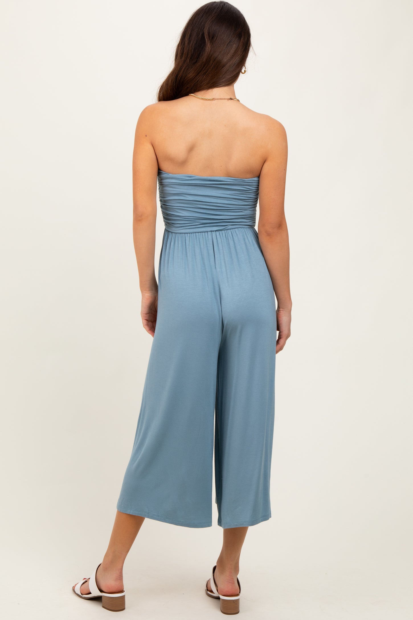 woman wearing a back view of a light blue strapless jumpsuit with a fitted bodice and wide-leg pants