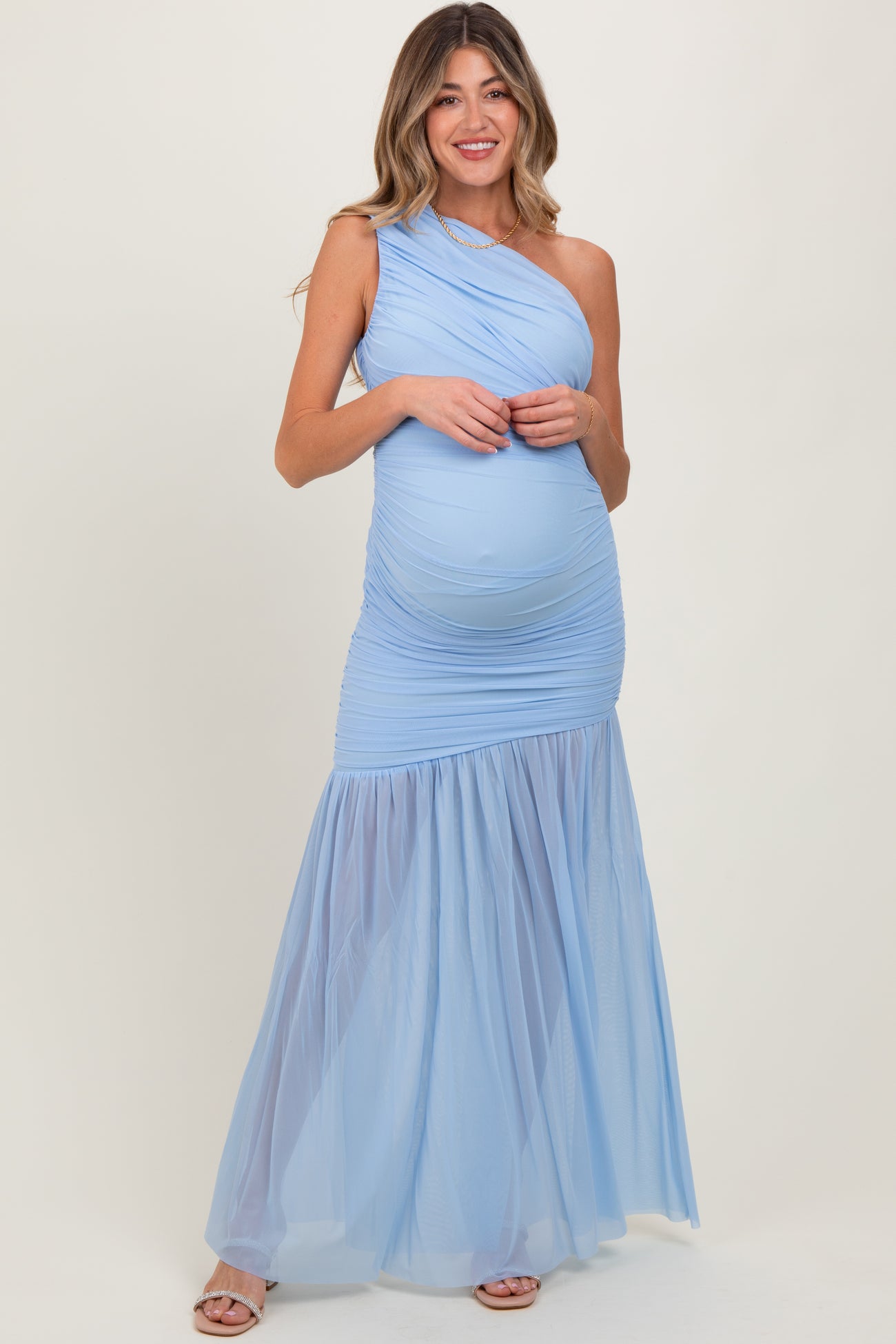 woman wearing a light blue one-shoulder maternity gown with ruched top and tulle skirt, showcasing her baby bump