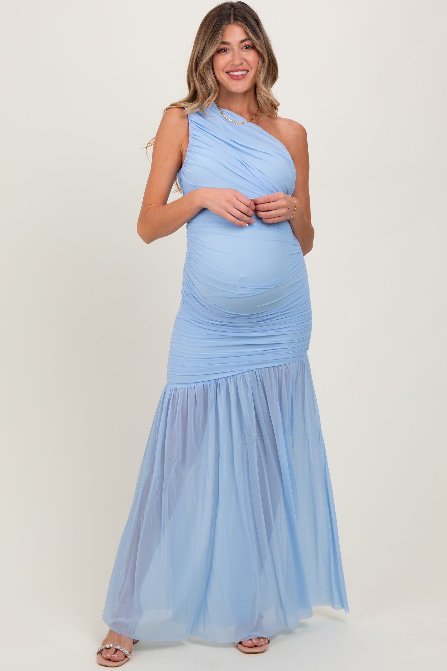 woman wearing a light blue one-shoulder maternity gown with ruched top and tulle skirt, showcasing her baby bump