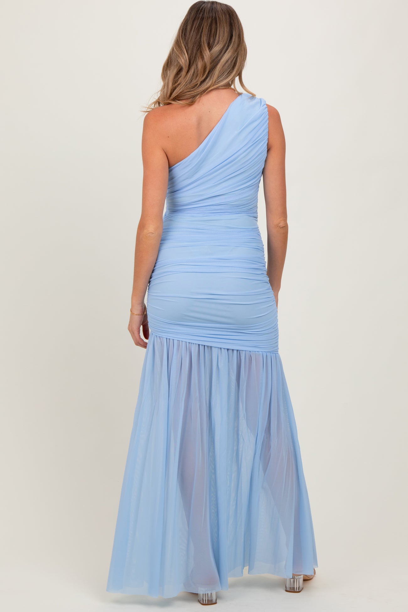 woman wearing a light blue one-shoulder maternity dress with ruched detailing and a flowy tulle skirt
