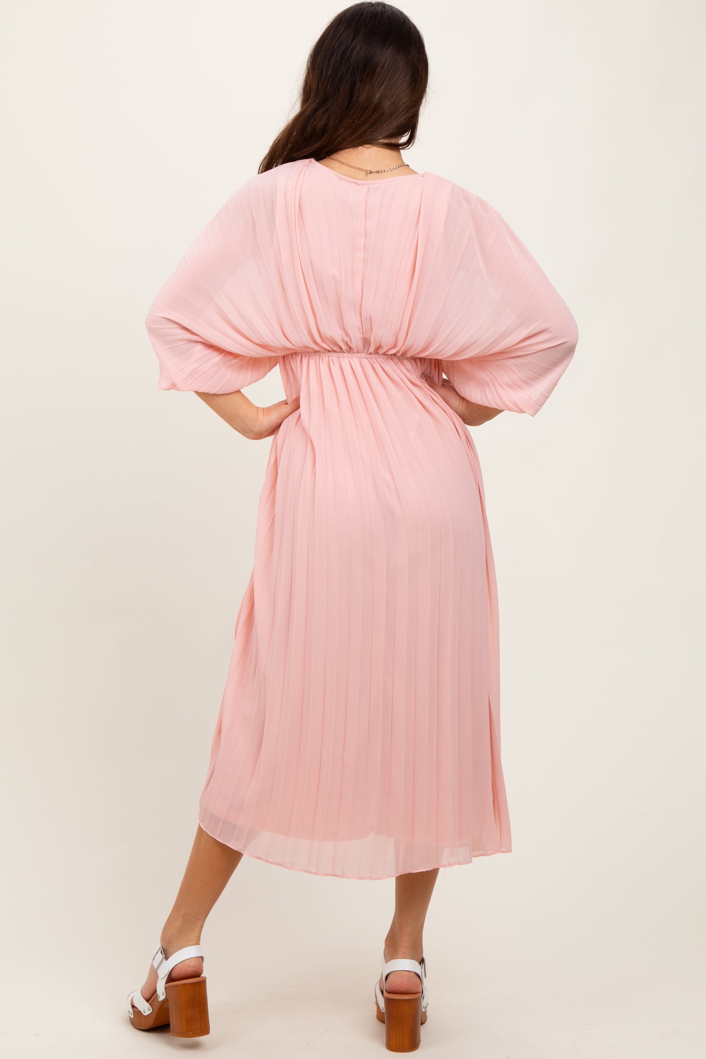woman wearing a pink pleated midi dress with batwing sleeves, showing the back and cinched waist